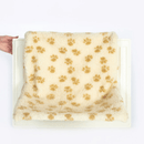 White background with a white radiator shown with a hand touch the side of it, on the radiator is a cream radiator cat bed with brown pawprints. 