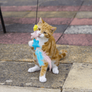 Ginger tabby cat with white paws playing with pastel coloured stars with feathers attached to a fishing rod style cat teaser.