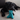 Black Labrador puppy lying with blue latex teddy bear dog toy in it's mouth while on carpet.
