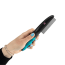 White background with a hand holding a blue and black Mikki Deluxe Flea Comb with metal teeth and a small pink 'M' on the handle. 