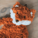 Close up of orange fox shaped dog toy with white chin and stitched detail eyes, brown nose, tags removed, pictured on a wooden floor. 