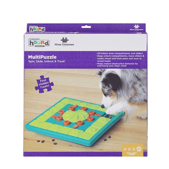 The retail packaging box for a MultiPuzzle dog toy by Nina Ottosson. The box features a purple and white design with a photo of a black and white dog interacting with the green and teal puzzle toy on a wooden floor.