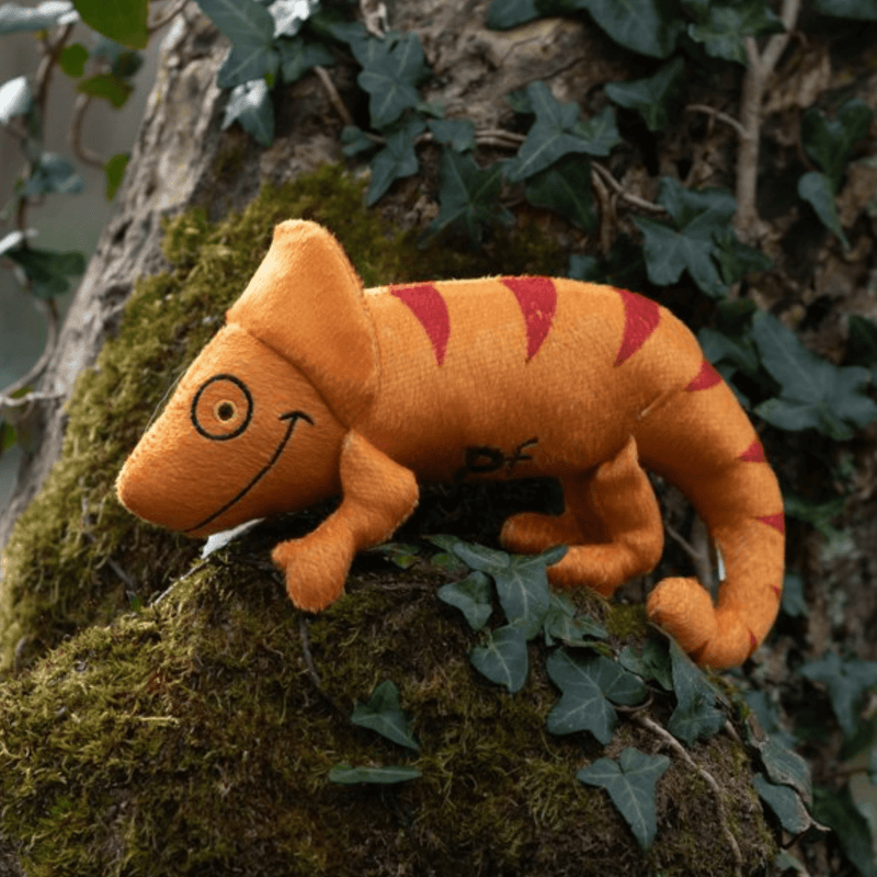 Orange plush Chameleon Cat toy with red stripe and eye and smile stitch details outside on a tree. 