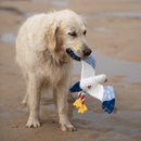 Golden Retriever dog with seagull dog toy with a white body, grey and blue wings and tail and orange beak in it's mouth standing on a beach. 