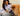 Woman sitting on a couch with a dog, holding a pouch of Pooch & Mutt Skin & Coat dog treats, against a neutral background.