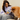 Woman sitting on a couch with a dog, holding a pouch of Pooch & Mutt Skin & Coat dog treats, against a neutral background.