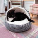 Black and white adult cat curled up in a grey cord and cream plush fabric cat cave pictured in a living room environment. 