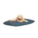 Sandy coloured Cockerpoo lying on a pillow-type blue dog bed with illustrated stags pictured on a white background. 