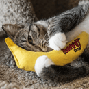Brown Tabby and white cat playing with Fabric yellow banana shaped cat toy with green labelled attached picturing a yellow cat with a Tutti Fruitti hat with text 'Yeowww!' coming from its mouth and 'Banana' written below. Lying on a beige fleece. 